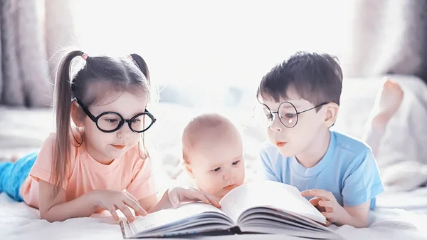 Kinderen liggen op het bed naast de pasgeboren baby, zusje. — Stockfoto