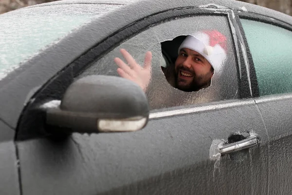 Homem em um boné vermelho de Papai Noel em um carro com vidro quebrado — Fotografia de Stock