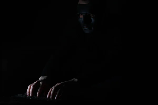 Człowiek w masce drukuje na klawiaturze w ciemności — Zdjęcie stockowe
