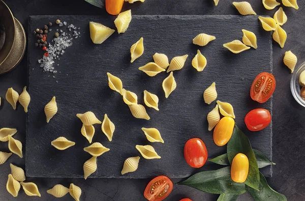 Cáscaras de pasta sobre piedra negra. Tomates y hojas de laurel con allspi — Foto de Stock