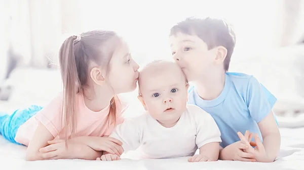 Los niños se acuestan en la cama junto al bebé recién nacido, hermanita . —  Fotos de Stock