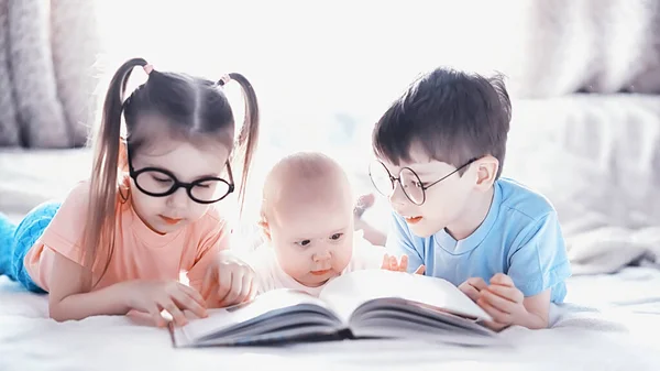 Kinderen liggen op het bed naast de pasgeboren baby, zusje. — Stockfoto