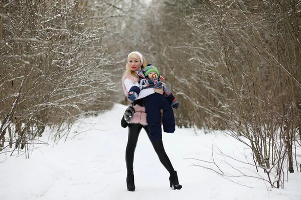 Madre joven camina en un día de invierno con un bebé en sus brazos en th — Foto de Stock