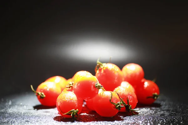 Tomates cherry sobre fondo negro en spray —  Fotos de Stock