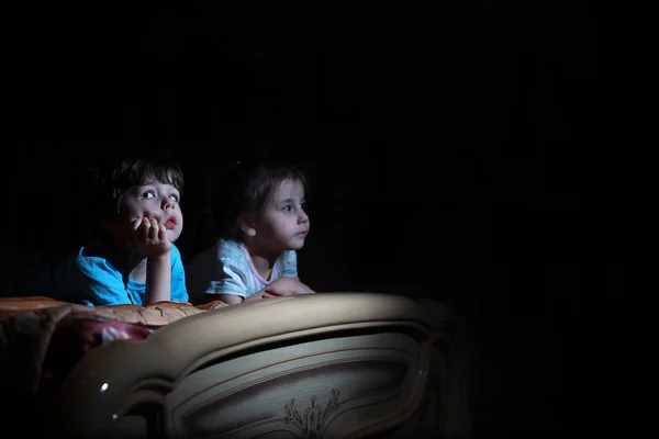 Niños pequeños en una habitación oscura viendo la televisión —  Fotos de Stock