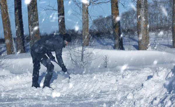 Человек убирает снег лопатой с дороги в снежную зиму — стоковое фото