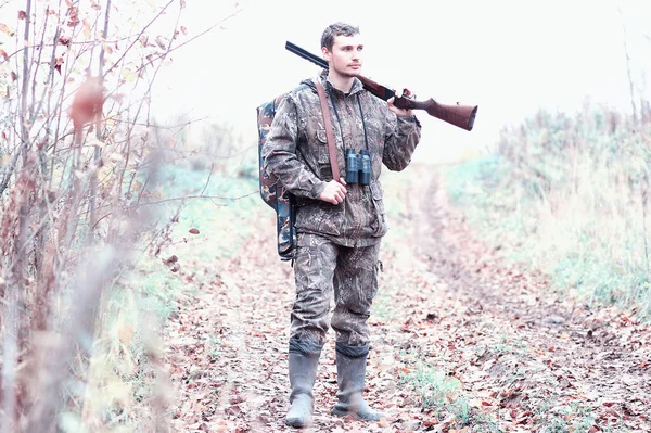 Un hombre en camuflaje y con un rifle de caza en un bosque en una sp — Foto de Stock