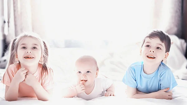 Kinderen liggen op het bed naast de pasgeboren baby, zusje. — Stockfoto