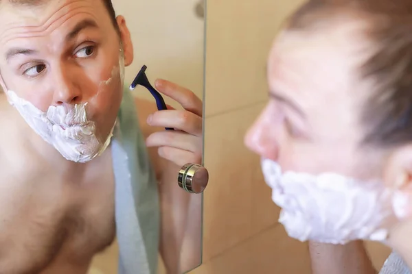 Een man scheert zich 's morgens in de badkamer. — Stockfoto