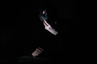 Maskeli bir adam karanlıkta klavyeye baskı yapmış.