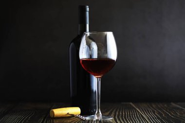 Masada bir bardak kırmızı kuru şarap. Siyah şişe ve bir bardak W