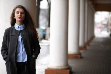 Genç, güzel bir kız, elinde bir sütunla binanın yanında yürüyor.