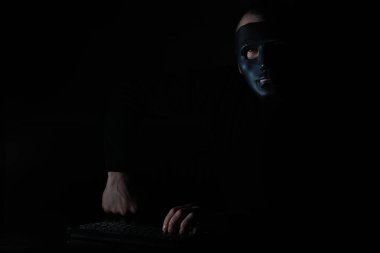 Maskeli bir adam karanlıkta klavyeye baskı yapmış.