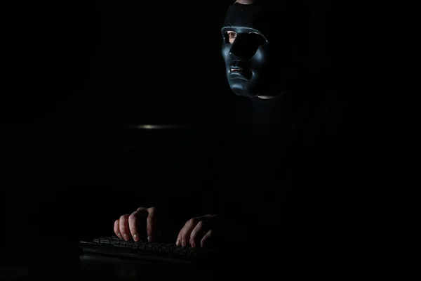 Un hombre con una máscara imprime en el teclado en la oscuridad — Foto de Stock