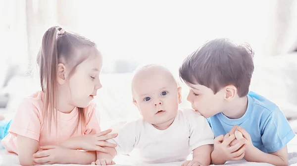 Los niños se acuestan en la cama junto al bebé recién nacido, hermanita . —  Fotos de Stock