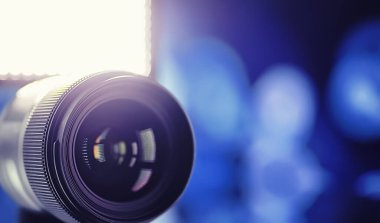 Ekipman kameramanı ve fotoğrafçı. Masadaki lensler parlak lambaların arka planına karşı. Kamera camının yansımasında parla ve bokeh.