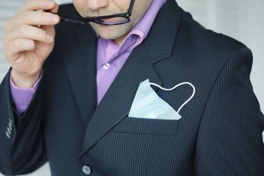 Tek kullanımlık bir tıbbi maske peçeteden sarkıyor. Takım elbiseli ve kot pantolonlu tek kullanımlık maskeli bir adam. Bireysel solunum koruması.