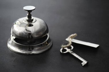 Otel resepsiyonunda parlak gümüş bir metal zil. Otel odasındaki masada bir zil ve kapı anahtarıyla birlikte bir masa. Anahtar ve zil bir otelde..