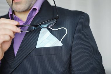 Tek kullanımlık bir tıbbi maske peçeteden sarkıyor. Takım elbiseli ve kot pantolonlu tek kullanımlık maskeli bir adam. Bireysel solunum koruması.