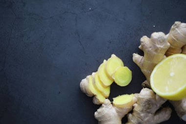 Zencefil kökü bütün ve dilimlenmiş. Koyu arkaplanda limonlu zencefil çayı. Taş zeminde taze zencefil kökü. Vitaminler. Üst Manzara. Metnin için boş yer.