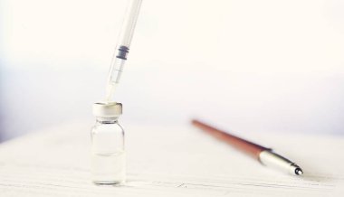 Bir adam tıbbi belge imzalıyor. Tıbbi ekipmanlar masada. Stetoskop ve şırıngalı ampuller. Ofiste notlar alıyor. Tıp Merkezi.