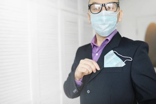 A disposable medical mask sticks out of a pocket instead napkin. A man with a disposable mask in a suit and jeans. Individual respiratory protection.