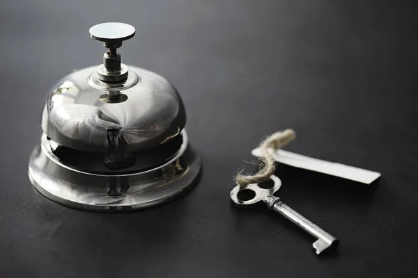 A shiny silver metal bell at hotel reception. A table in the hotel at the concierge with a bell and a door key. Key and bell in a hotel.