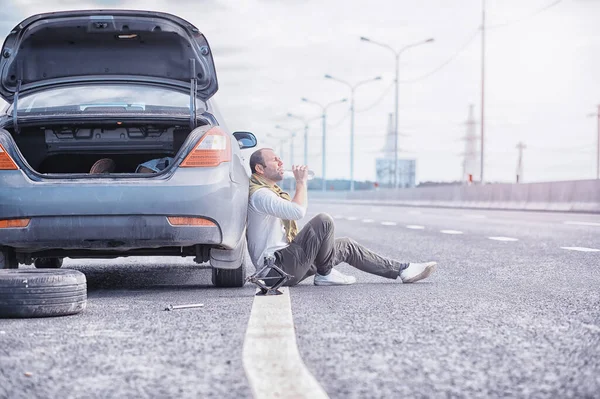 道路上の車のホイールを交換します タイヤの仕事をしてる男が — ストック写真