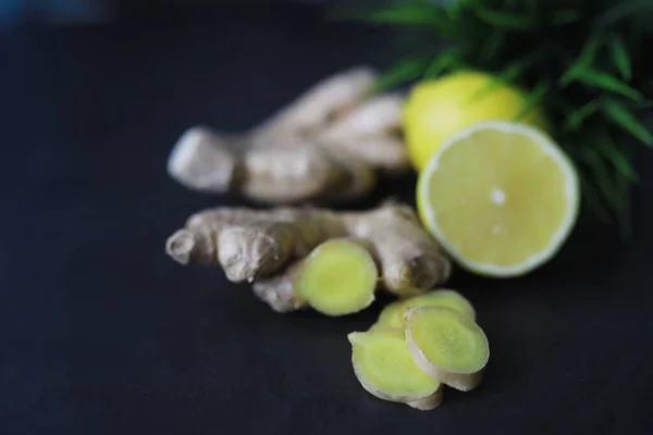 Ginger root whole and sliced. Ginger tea with lemon on the dark background. Fresh ginger root on stone background. Vitamins. Top view. Free space for your text.