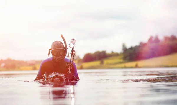 A scuba diver in a wet suit prepares to immerse in a pond