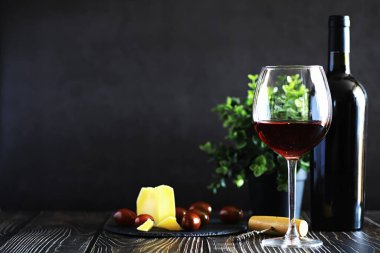 Masada bir bardak kırmızı şarap. Siyah şişe ve bir bardak şarap..