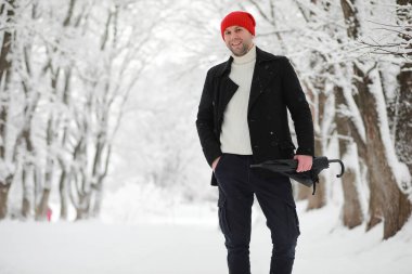 Parkta yürüyen bir adam. Kışın kar altında şemsiyeli genç bir adam..