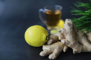 Zencefil kökü bütün ve dilimlenmiş. Koyu arkaplanda limonlu zencefil çayı. Taş zeminde taze zencefil kökü. Vitaminler. Üst Manzara. Metnin için boş yer.