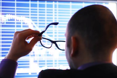Bir işadamı monitördeki bir grafiğe bakıyor. Borsa simsarı borsa eğilimlerini değerlendirir. Ekonominin dinamiklerinin önünde gözlüklü bir adam..