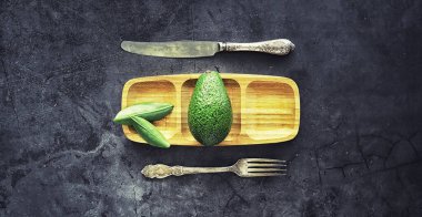 Avokado yemek tarifleri. Tahta kesme tahtasında servis edilen olgun yeşil avokado..
