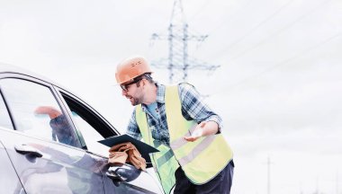 Kasklı ve üniformalı bir adam, sahada bir elektrikçi. Profesyonel elektrik mühendisi elektrik hatlarını inceliyor..