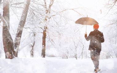 Parkta yürüyen bir adam. Kışın kar altında şemsiyeli genç bir adam..