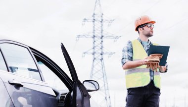 Kasklı ve üniformalı bir adam, sahada bir elektrikçi. Profesyonel elektrik mühendisi elektrik hatlarını inceliyor..