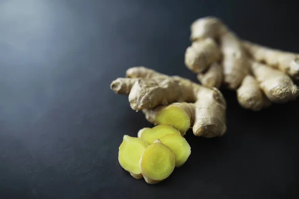 Ginger root whole and sliced. Ginger tea with lemon on the dark background. Fresh ginger root on stone background. Vitamins. Top view. Free space for your text.