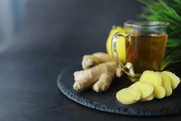 Ginger root whole and sliced. Ginger tea with lemon on the dark background. Fresh ginger root on stone background. Vitamins. Top view. Free space for your text.