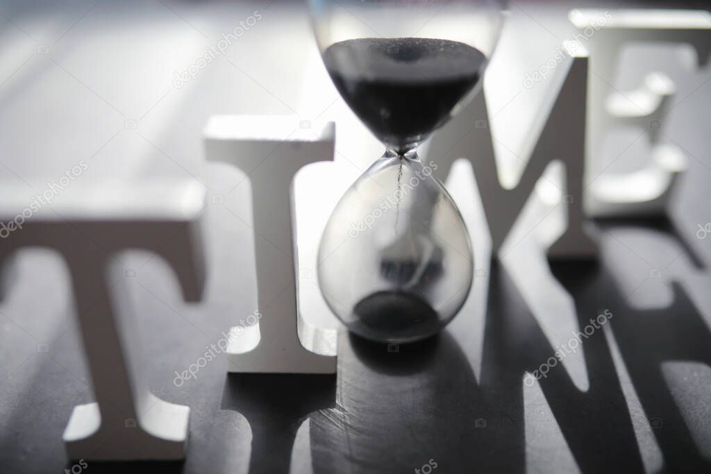 The concept of the passage of time. Hourglass on a dark background. Inscription time. The shadow on surface of the word.