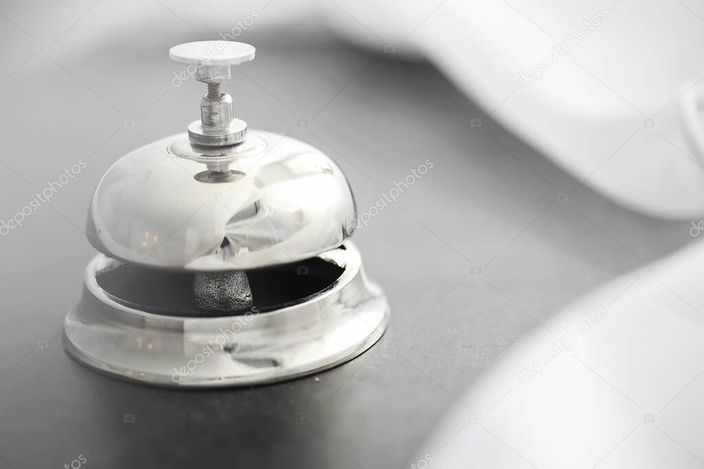 A shiny silver metal bell at hotel reception. A table in the hotel at the concierge with a bell and a door key. Key and bell in a hotel.