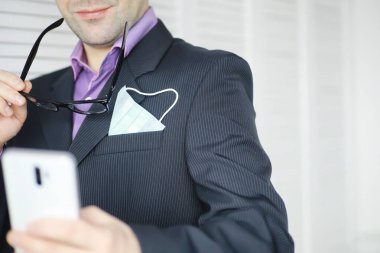 Tek kullanımlık bir tıbbi maske peçeteden sarkıyor. Takım elbiseli ve kot pantolonlu tek kullanımlık maskeli bir adam. Bireysel solunum koruması.