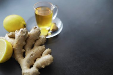 Zencefil kökü bütün ve dilimlenmiş. Koyu arkaplanda limonlu zencefil çayı. Taş zeminde taze zencefil kökü. Vitaminler. Üst Manzara. Metnin için boş yer.