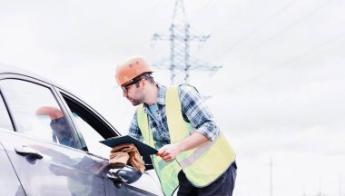 Kasklı ve üniformalı bir adam, sahada bir elektrikçi. Profesyonel elektrik mühendisi elektrik hatlarını inceliyor..