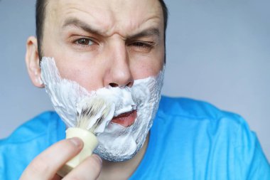 Bir adam aynanın önünde tıraş olur. Tıraş köpüğü. Tek kullanımlık jilet..