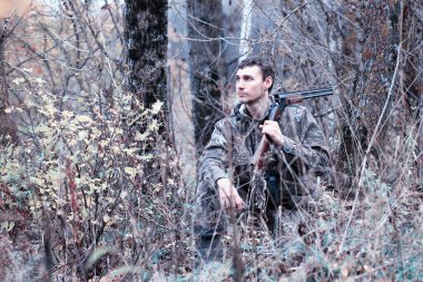 Kamuflajlı bir adam ve elinde av tüfeğiyle bir bahar köpeğinin üzerinde bir ormanda.