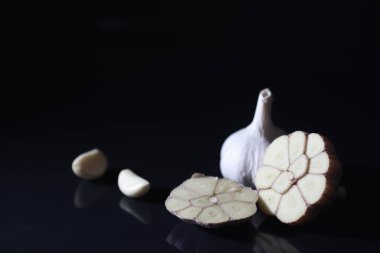 Siyah arka planda taze sarımsaklı karanfil. Sarımsak vitamin açısından zengindir, kullanışlı bahar, iyi baharatlar. Karanlık bir arka planda dilimlenmiş sarımsak. Çiğ sarımsak..