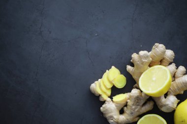 Zencefil kökü bütün ve dilimlenmiş. Koyu arkaplanda limonlu zencefil çayı. Taş zeminde taze zencefil kökü. Vitaminler. Üst Manzara. Metnin için boş yer.
