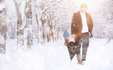 Parkta yürüyen bir adam. Kışın kar altında şemsiyeli genç bir adam..